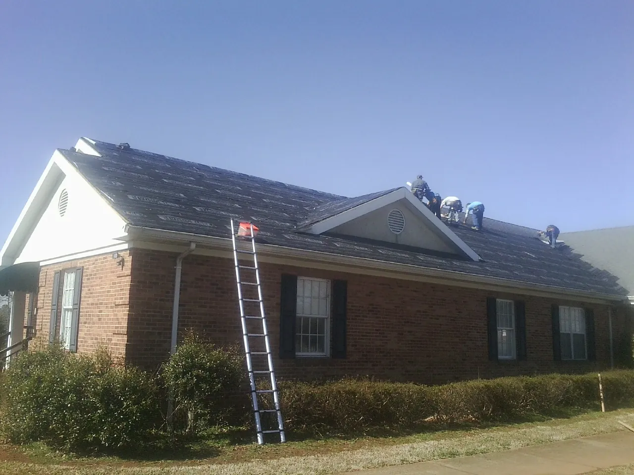 Crew tearing shingles off a brick ranch roof with a ladder set — Metal Roof Repair work by our crew in Fishtail