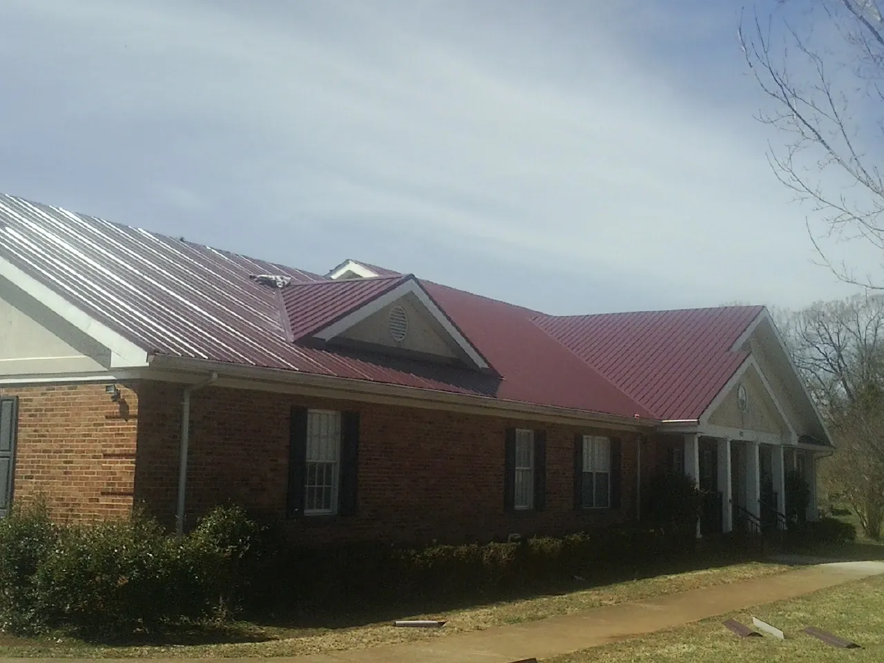 Red metal roof with gabled entries on a long brick building, from a Hail Damage Roof Repair job in Fishtail