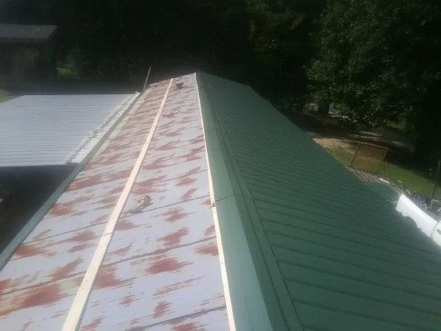 Old rusted panels beside newly installed green metal roofing — Wind Damage Roof Repair by Roofing Brothers in Fishtail