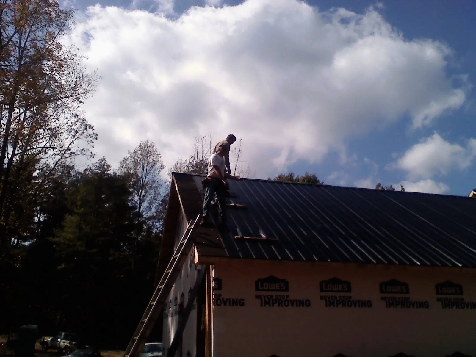 Roofer fastening dark metal panels high against a cloudy sky, from a Roof Inspection job in Fishtail