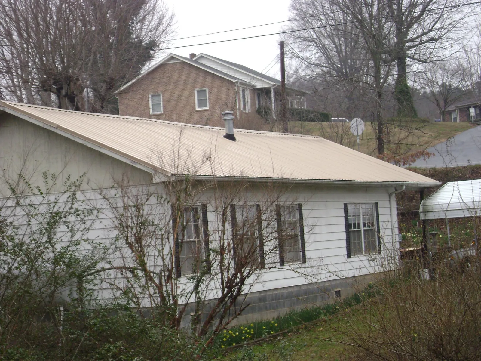 Tan metal roof on a white sided house set into a hillside — Commercial Roofing by Roofing Brothers in Fishtail